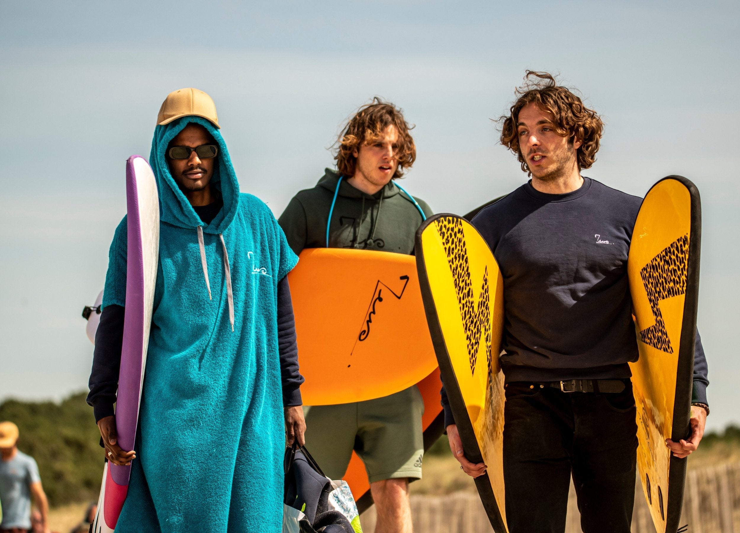 Un groupe de surfeurs en train de marcher avec des planches de surf et des ponchos de surf