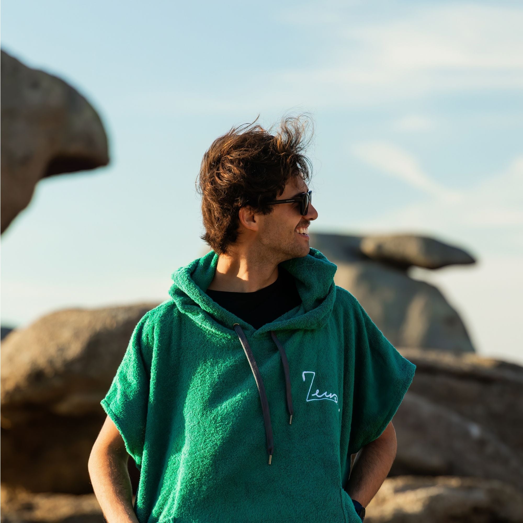 a man wearing a green hoodie standing in front of a rock formation