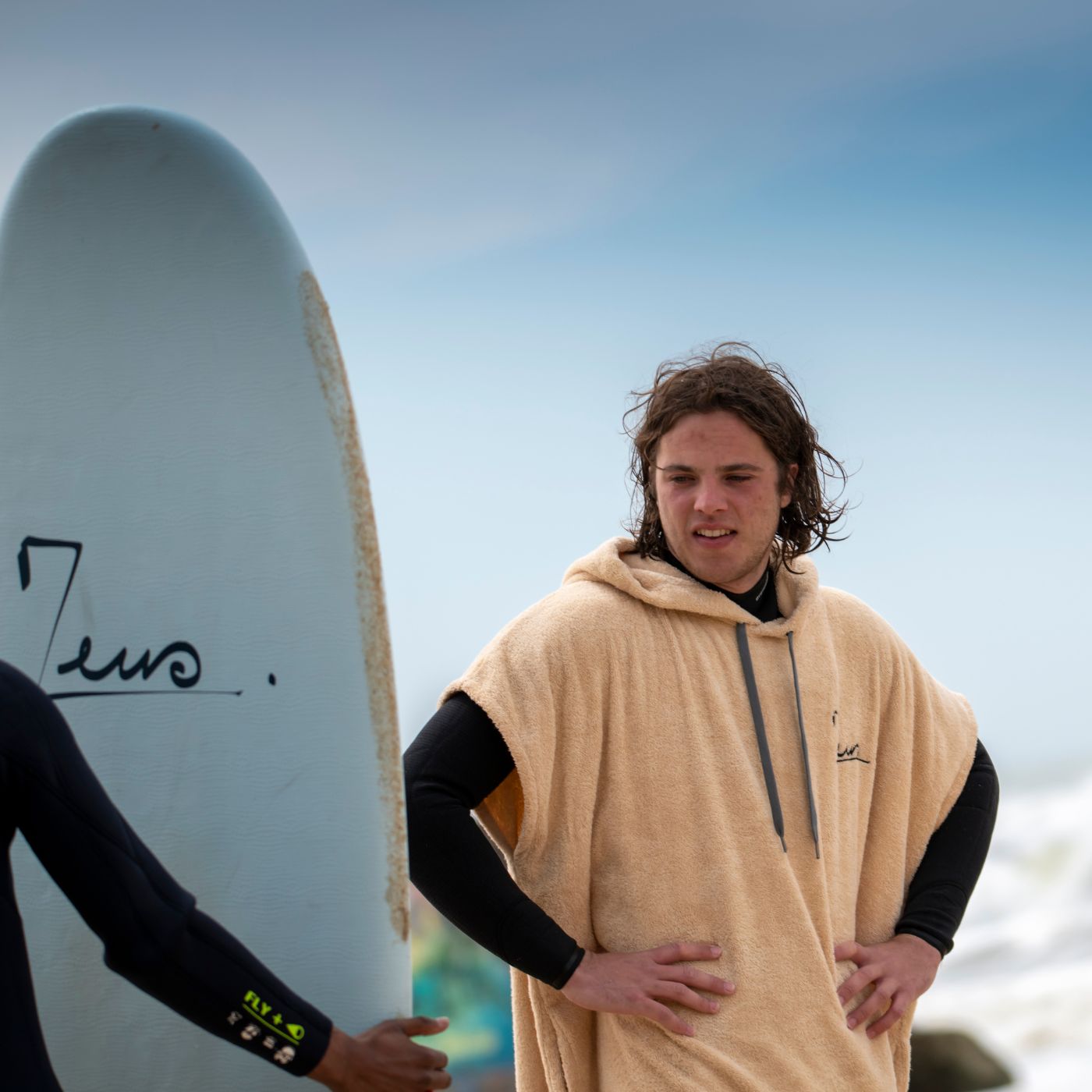 a man standing next to another man holding a surfboard